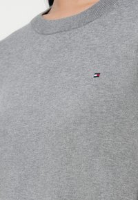 Szary sweatshirt wykonany z miękkiego materiału, z okrągłym dekoltem i małym haftowanym logo w kolorach czerwonym, białym i niebieskim na piersi.