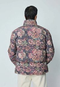 Veste rembourrée florale avec un fond sombre et de grandes fleurs roses, crème et vertes ; design matelassé ; col haut ; matériau léger.