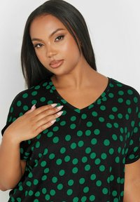 Mustapaita vihreillä pilkuilla, V-kaula-aukolla, lyhyillä hihoilla ja teksturoidulla kankaalla. Ominaisuuksiin kuuluu rento malli ja hienovarainen sauma.