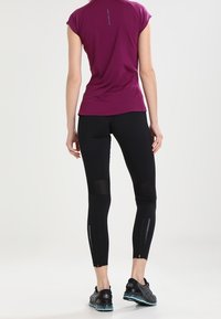 Träningsoutfit med en åtsittande, kortärmad, vinröd topp och svarta leggings med nätpaneler och reflekterande detaljer. Svarta sneakers fulländar looken.