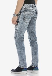 Verblasste blaue Jeans im Slim-Fit, mit einem Fünf-Taschen-Design und strukturiertem Waschverfahren. Detaillierte Nähte und ein zerknitterter Look sind sichtbar.