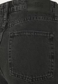 Černé džíny z denimu s zadní kapsou a koženou etiketou s textem "BDG". Tkanina má hladkou strukturu a mírně vybledlý vzhled.