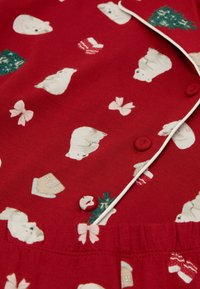 Červený pyžamový set z látky s potiskem polárních medvědů, mašlí, vánočních dárků a stromů. Obsahuje knoflíky a elastický pas.