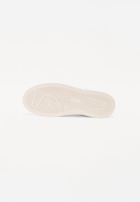 Suola di una sneaker in gomma beige chiaro, caratterizzata da un motivo a spina di pesce testurizzato per la trazione e bordi arrotondati, posizionata su uno sfondo bianco.