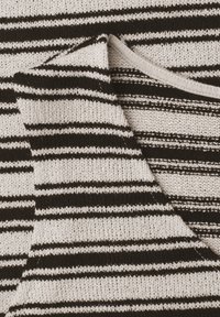 Gros plan sur un tissu tricoté plié avec des rayures horizontales noires et blanches créant un motif texturé.