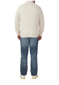 Sweatshirt beige clair avec un col montant, poignets et taille côtelés, associé à un jean en denim bleu et des baskets blanches.