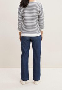 Randig grå och vit långärmad topp med rundad halsringning, kombinerad med mörkblå vida jeans och vita sneakers. Slätt, mjukt tyg.