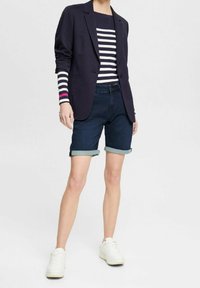 Blazer navy, camisa de rayas de manga larga con acentos rosas, pantalones cortos de denim doblados en el dobladillo y zapatillas blancas. Conjunto casual y en capas.