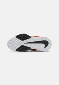 Suela de zapatilla con una superficie texturizada blanca y acentos de goma negra, que muestra un diseño de logo curvado y un patrón de tracción multidireccional.
