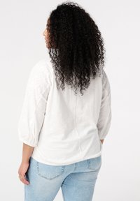 Weiße, strukturierte Bluse mit Ballonärmeln und Rundhalsausschnitt, kombiniert mit hellblauen Jeans. Minimalistisches Design, keine sichtbaren Muster.