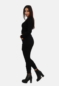  Schwarzes, geripptes Langarm-Crop-Top, kombiniert mit schwarzen Cargo-Hosen. Das Outfit wird durch schwarze, knöchelhohe Stiefel mit strukturiertem Design ergänzt.