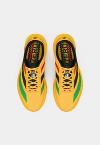 Chaussures de course jaune vif avec des accents noirs, verts et rouges, lacées et vues de dessus sur un fond blanc.