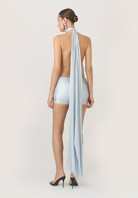 Világoskék pánt nélküli top, hosszú, lágyan áramló hátrésszel, felszerelve testhezálló sorttal; puha textúra és elegáns dizájn jellemzi. A megjelenést magassarkú szandálok egészítik ki.