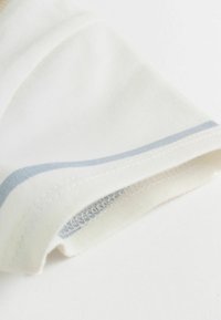 Bela bombažna tkanina, ki prikazuje manšeto s svetlo modrimi črtami in fino šivano podrobnostjo. Mehka, gladka tekstura s čistim zaključkom.