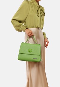 Borsa a tracolla verde con texture, chiusura liscia, forma rettangolare, manico corto e logo discreto su un'etichetta argentata.