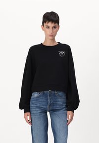 Melna cropped džemperis ar garām bumbieru piedurknēm, ar sudraba logotipa detaļu uz kreisā krūšu. Viegls audums ar gludu tekstūru.