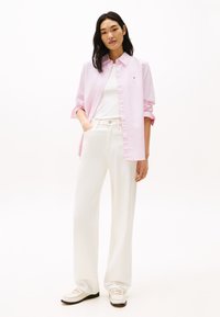 Camicia a righe rosa chiaro con bottoni sopra una t-shirt bianca aderente, abbinata a pantaloni bianchi a gamba larga e mocassini crema con accenti dorati.