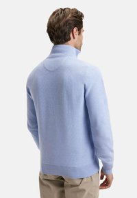 Pull en tricot bleu clair avec un col haut, des bords côtelés aux poignets et à l'ourlet, présentant une finition texturée et un design sans couture à l'arrière.