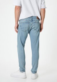 Jeans de mezclilla azul claro con corte recto, cinco bolsillos y una etiqueta de cuero en la cintura trasera; combinados con zapatillas blancas.