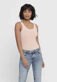 Light pink sleeveless tank top in a fitted design, paired with light blue denim jeans. Smooth fabric with subtle stretch.