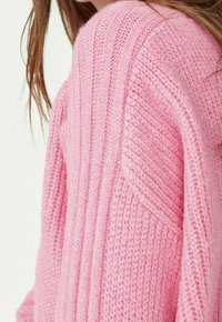Maglione rosa lavorato a maglia con una texture a coste, vestibilità ampia e spalle scese, con cuciture visibili e un aspetto morbido e accogliente.
