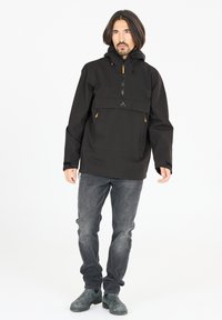 Veste pullover noire avec une poche à l'avant, un col zippé et une capuche avec cordon de serrage. Présente des accents marron sur la poche et les poignets. Jean gris et bottes.