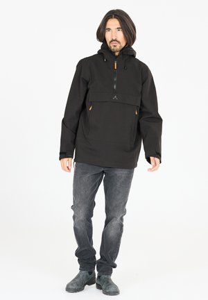 Sort pulloverjakke med en frontlomme, lynlåshals og snoretræk i hætten. Har brune detaljer på lommen og manchetterne. Grå jeans og støvler.