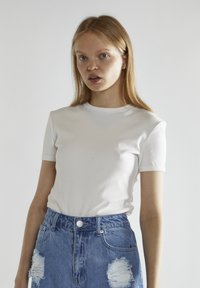 T-shirt bianca a maniche corte in cotone, con collo rotondo e vestibilità slim. Abbinata a pantaloni shorts in denim blu strappati a vita alta.