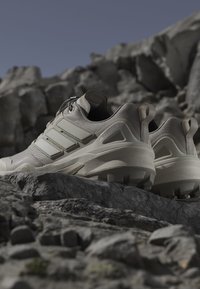 Beige athletic shoes with textured fabric and rubber soles, featuring three distinctive stripes and a reinforced heel for stability.