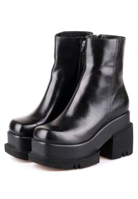 Paire de bottines en cuir noir brillant avec talons plateformes épais et fermetures éclair latérales sur fond blanc.