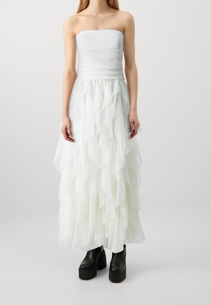 Robe blanche bustier avec un corsage ajusté et une jupe longue à volants superposés. La jupe présente des volants en couches pour la texture, assortie à des bottes plateformes noires.