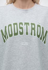 Sweat-shirt gris clair avec de grandes lettres vertes "MODSTRÖM" et un texte blanc plus petit "EST. 2004 COPENHAGEN" en dessous.