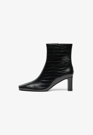 Stivale alla caviglia nero con punta affusolata, esterno lucido con texture a crocco e tacco quadrato di altezza media. Design liscio e elegante.