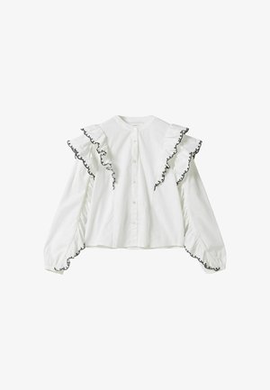 Blouse blanche à manches longues avec épaules et poignets volantés bordés d’une broderie noire, avec un boutonnage devant et un col rond.