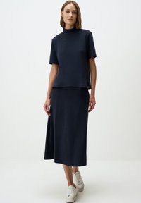 Ensemble deux pièces marine avec un haut à manches courtes et une jupe midi, fabriqué en tissu texturé. Associé à des baskets blanches.