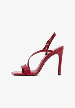 Red patent leather high-heeled sandal with a square toe, slim ankle strap, and crisscross design. Features a sleek, glossy finish.