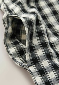 Tissu à carreaux noir et blanc avec une couture visible et une ouverture de manche pliée sur un fond neutre.