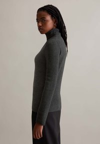 Gray ribbed turtleneck sweater with a fitted silhouette and long sleeves, paired with a dark pants. Texture appears soft and snug.