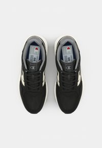 Black athletic sneakers with a mesh upper, featuring white stripes and black laces. A soft gray lining and a white rubber sole complete the design.