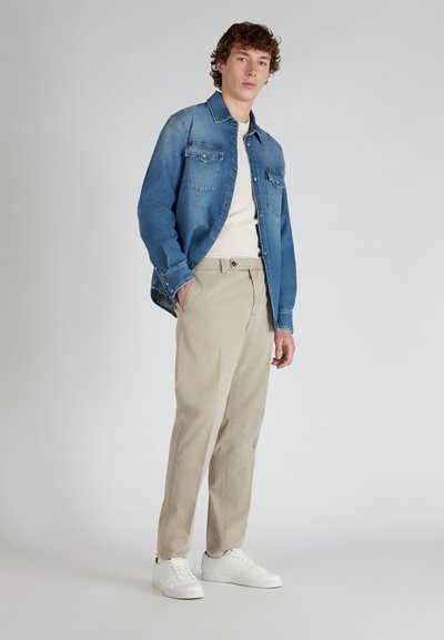 Blauwe denim overhemd met twee borstzakken, gecombineerd met lichtbeige broek en witte sneakers, wat een gelaagde casual look creëert.
