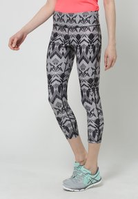 Černé a šedé legíny se vzorem, vysokým pasem a geometrickým designem. V páru s světle modrými atletickými botami.