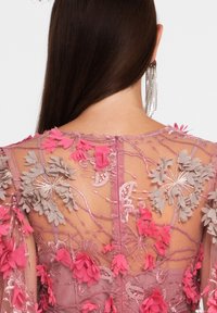 Lavendelfarbenes transparentes Stoff mit filigraner Blumenstickerei in Rosa und Grau, mit langen Ärmeln und einem zarten Detail am Rücken.