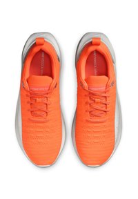 Scarpe da atletica di un vivace arancione con una tomaia texture, lacci e una suola grigia. Caratterizzate da una punta arrotondata e un design leggero e flessibile.