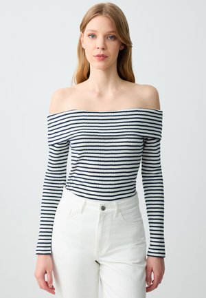 Schulterfreies, geripptes Oberteil mit navy- und weißen Streifen, mit langen Ärmeln und einer figurbetonten Passform. Kombiniert mit hoch taillierten weißen Hosen.