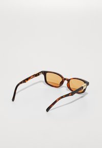 Ochelari de soare din scoică cu lentile maro, formă rectangulară și accente aurii pe brațe. Textură netedă și lucioasă.