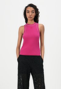 Débardeur rose ajusté sans manches avec un col rond et des accents argentés. Associé à un pantalon palazzo en dentelle noire présentant des motifs floraux.