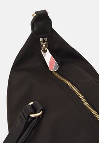 Black nylon bag featuring a gold zipper, a black leather strap, and a charm with a red, white, and blue design.