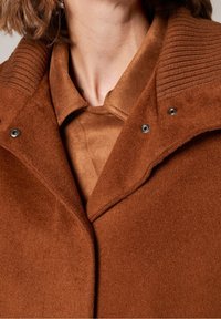 Abrigo de mezcla de lana marrón con un cuello acanalado texturizado, cierres a presión y una capa interior suave de un tono similar.