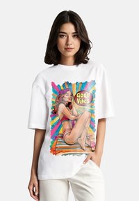 Witte oversized t-shirt met een grafisch ontwerp van een vrouw op een kleurrijke gestreepte achtergrond, met de tekst "Good Vibes" in vette letters.