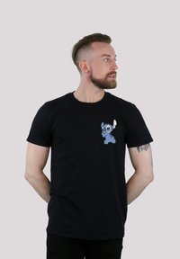 Svart bomull T-skjorte med en blå tegneseriefigur i venstre brystområde. Kortermet og rund halsdesign.